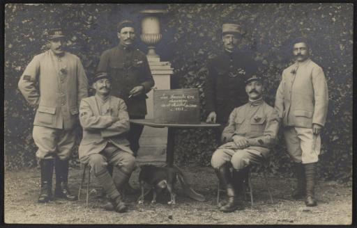 Six hommes en uniforme militaire autour d'une table où est posé un écriteau indiquant "Les Hercules C.P.C. chaumière de St Michel en l'Herm, 1918".