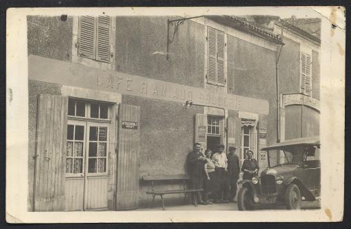 Le café R. Amiaud - sellerie. Sur le volet, "Autobus Brivin et Cie - arrêt" ; cinq personnes posent devant l'entrée, à côté d'une automobile.