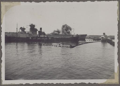 [Le cuirassé Jean Bart] tirant des salves, amarré dans le port de Casablanca derrière le cargo SS Ste Jacqueline, photographié depuis la tour de contrôle de la batterie militaire.