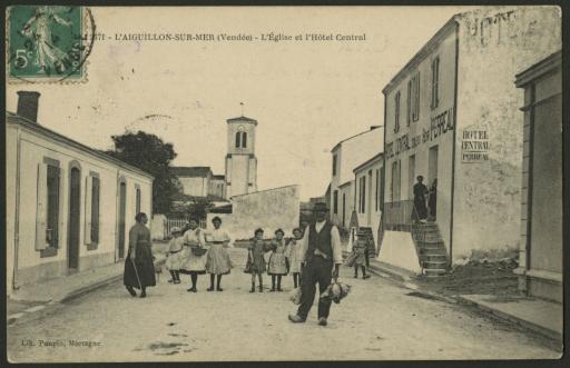 Un groupe de personnes prenant la pose dans la rue devant l'hôtel Central "Perreau", avec l'église en arrière-plan.