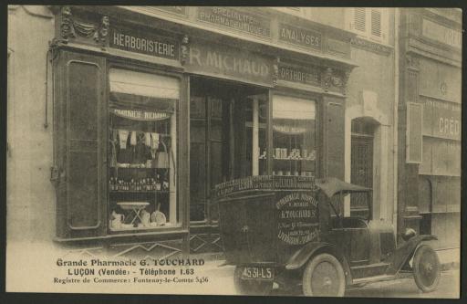 La devanture de la pharmacie R. Michaud, devenue la Grande Pharmacie Nouvelle G. Touchard, avec la voiture commerciale stationnée devant.