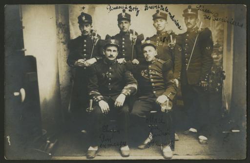 (1 Num 1/181/1). Photographie de Jean Auvrignon en uniforme du 114e régiment d'infanterie, avec cinq de ses camarades dont les noms et les domiciles sont écrits à l'encre. Jean est désigné par une croix.
