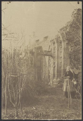 (213 J 95). Jeune paysanne devant la porte de l'ancienne chapelle de l'abbaye de la Blanche.